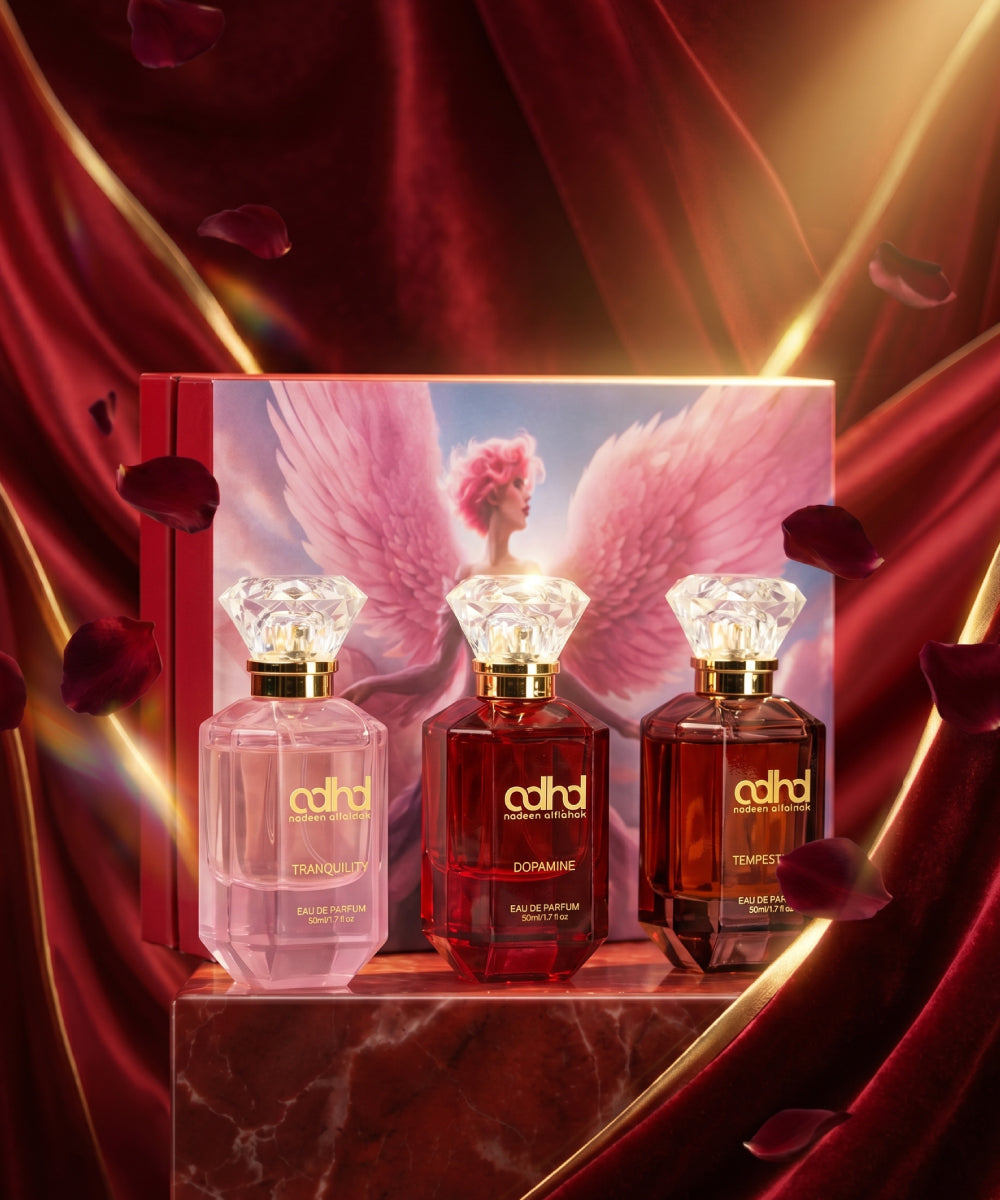 Three colored bottles with diamond shape caps in front of a rectangular box with the image of an angel with pink wings