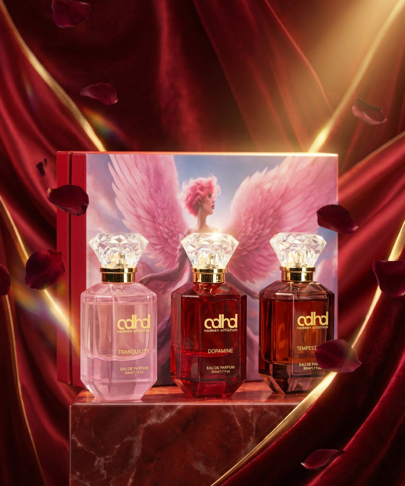 Three colored bottles with diamond shape caps in front of a rectangular box with the image of an angel with pink wings
